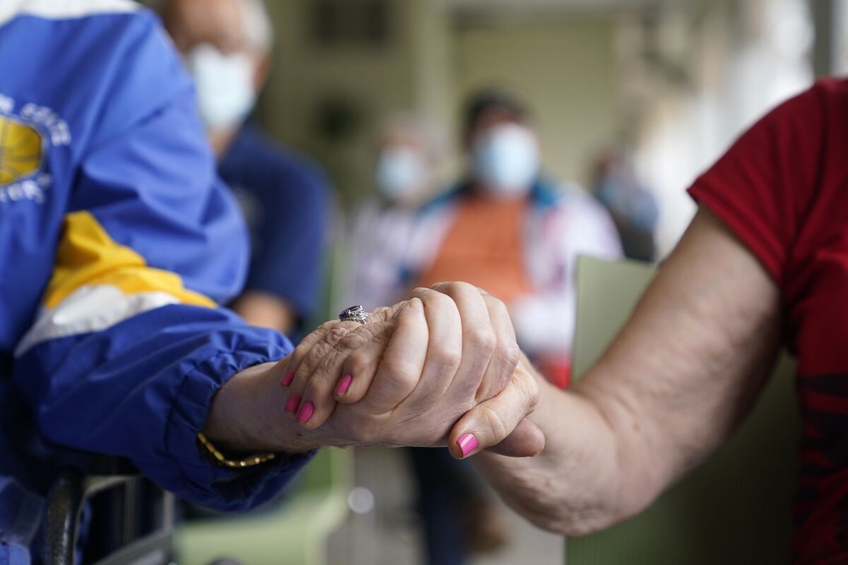 Two people hold hands as they wait for a COVID-19 vaccine