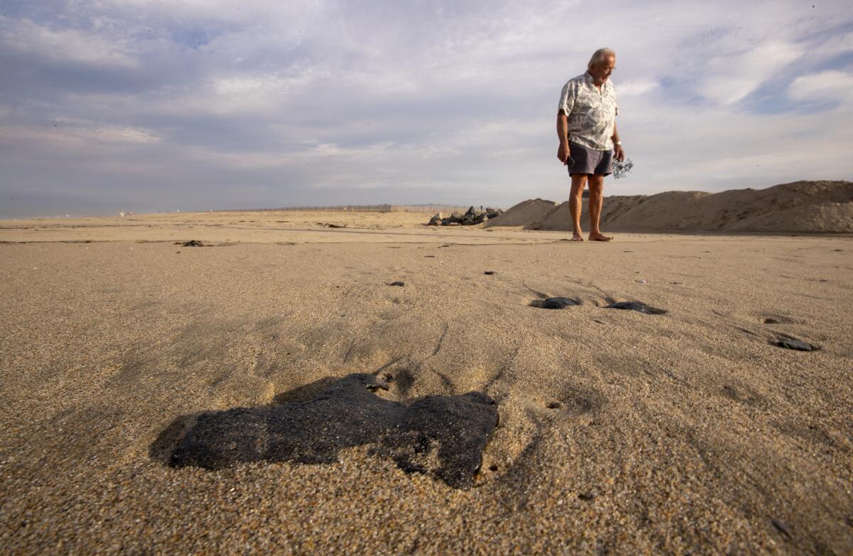 A person stands on the beach and looks down at the sand