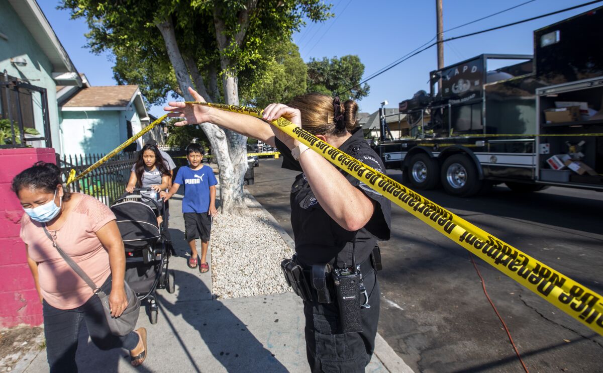 Police officer holds up yellow caution tape as people walk under it