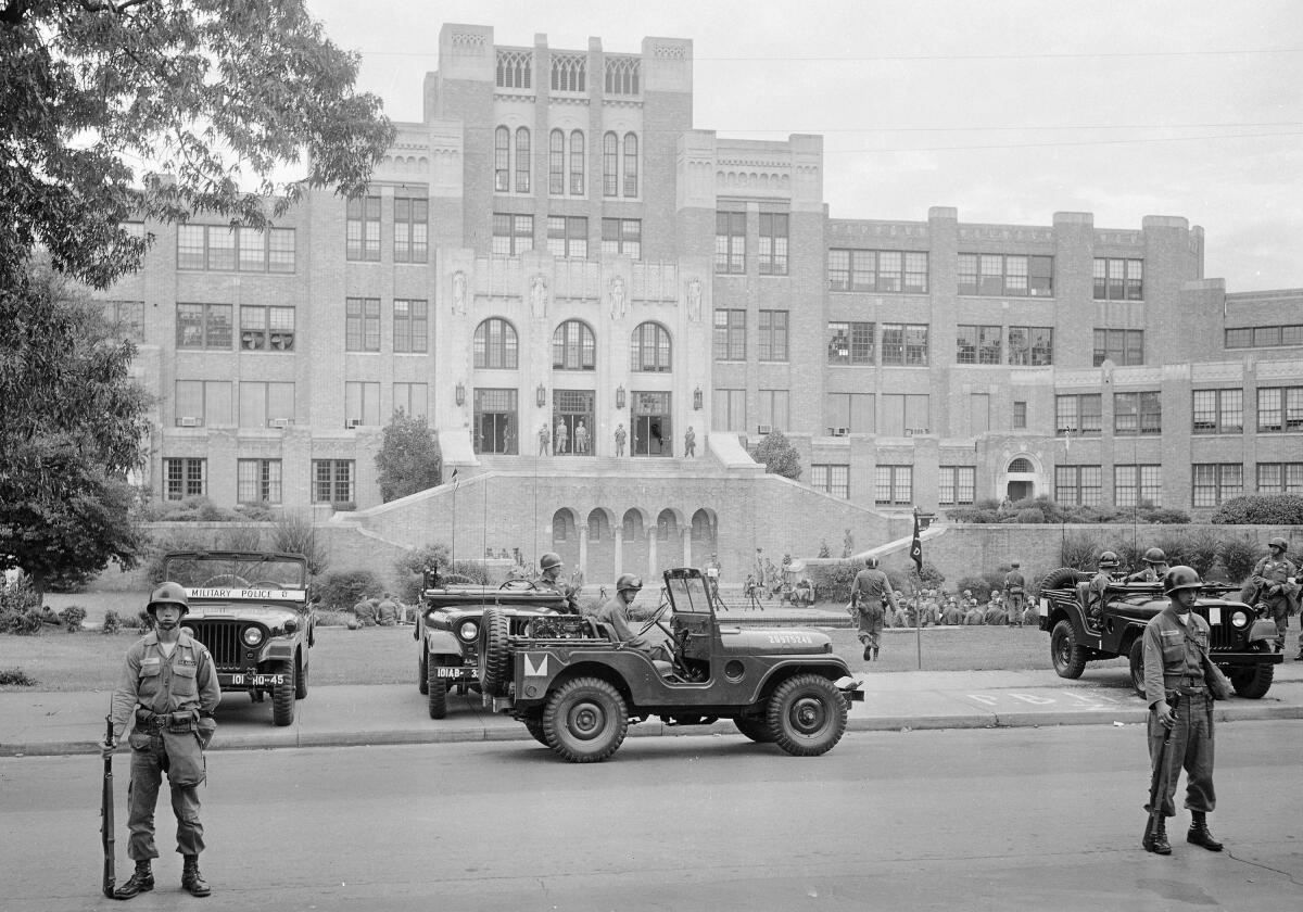 Soldiers and Army jeeps outside a high school building in a black-and-white photo 