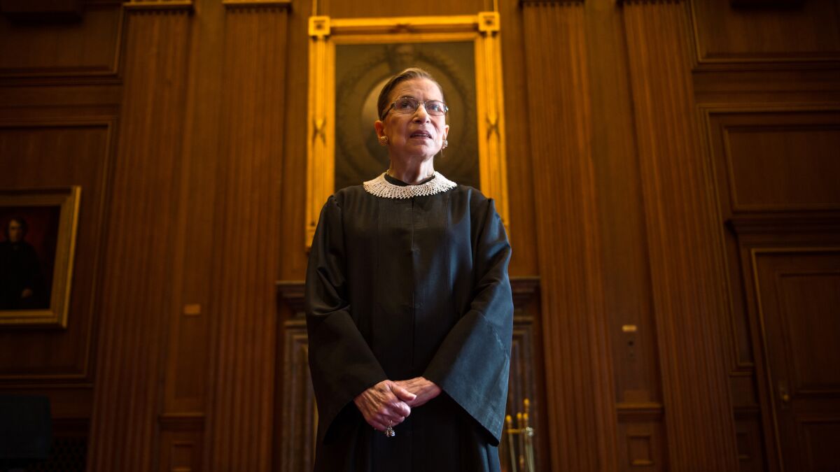 Justice Ruth Bader Ginsburg poses for a portrait standing in a wood-paneled conference room in the Supreme Court