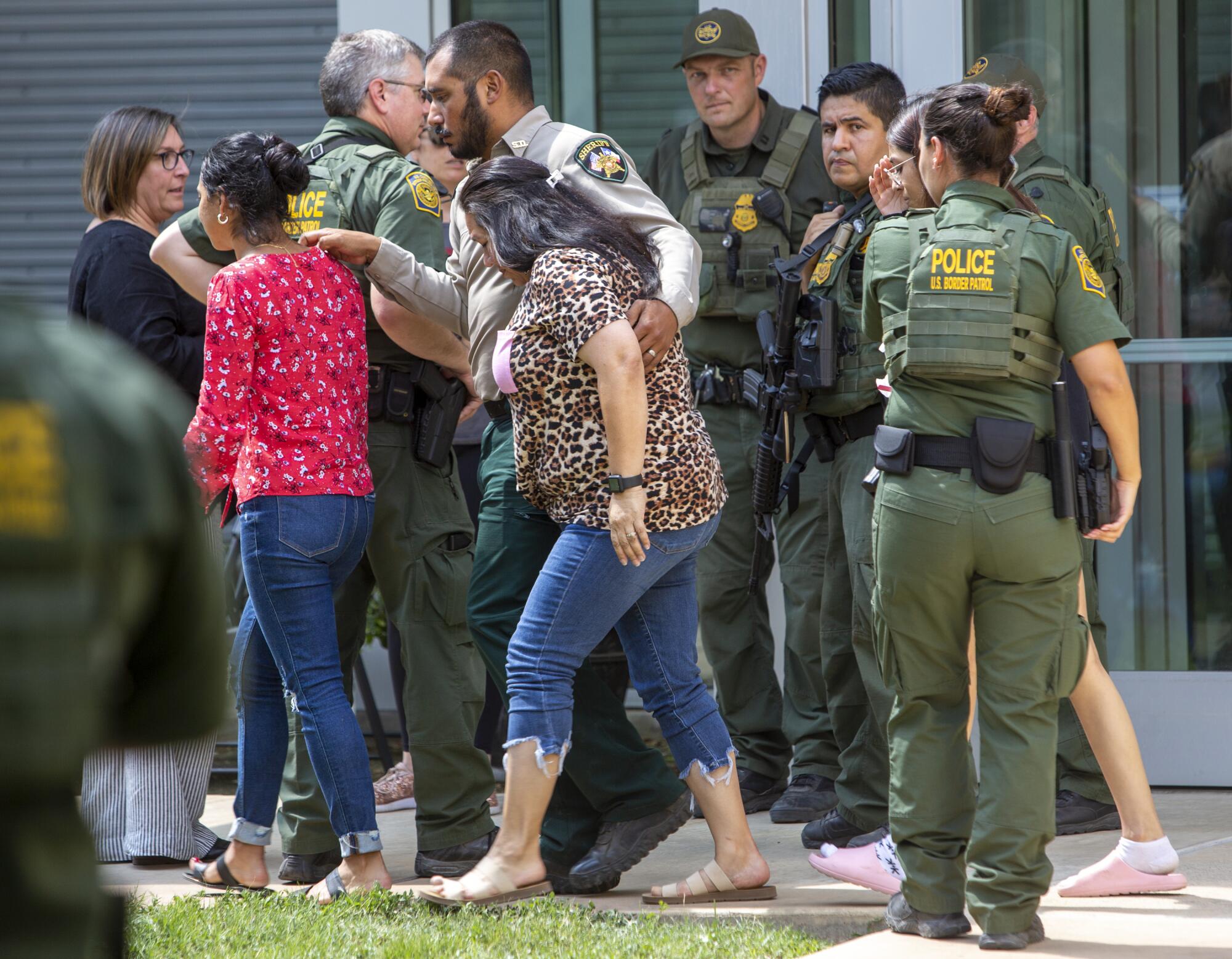 A man in uniform has his arm around a woman as they and another woman walk past law enforcement personnel in uniform