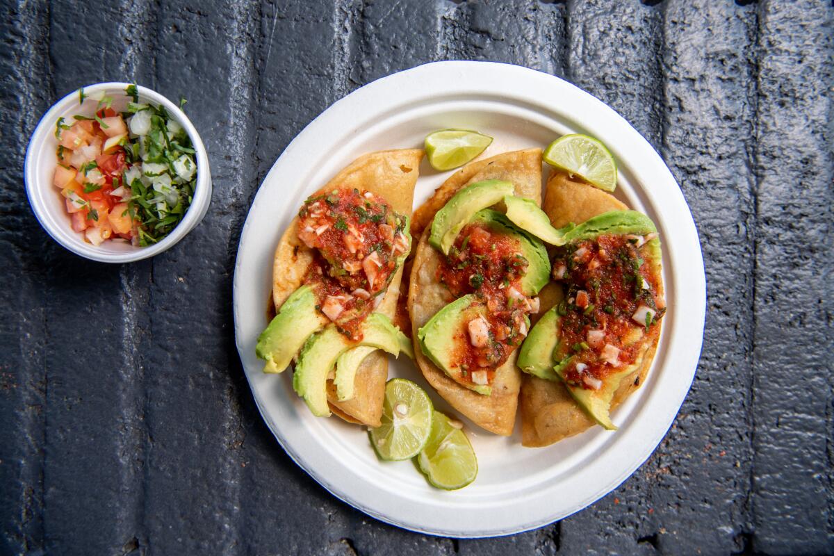 Mariscos Jalisco's tacos dorados de camaron on a plate with lime wedges and avocado slices.