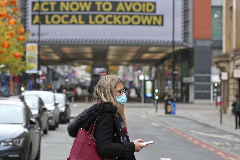 A woman wearing a face mask walks in Manchester, England, Monday, Oct. 19, 2020. Britain’s government says discussions about implementing stricter restrictions in Greater Manchester must be completed Monday because the public health threat caused by rising COVID-19 infections is serious and getting worse. (Peter Byrne/PA via AP)
