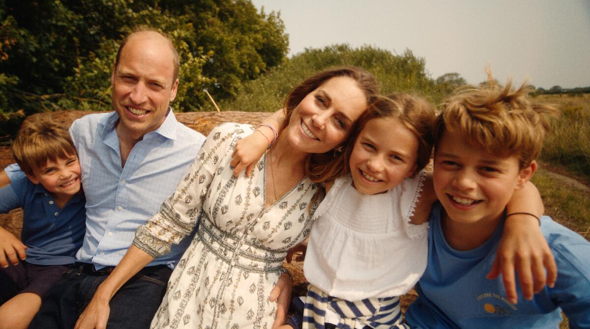 Catherine, Princess of Wales, sitting outdoors between her husband and their three children