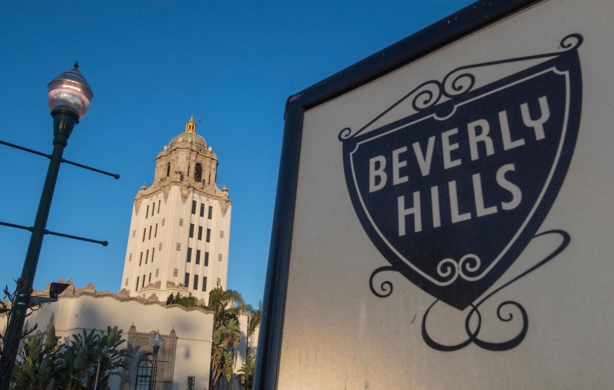 A view of a building with a tower in the background. In the foreground are a lamppost and a sign that says Beverly Hills 
