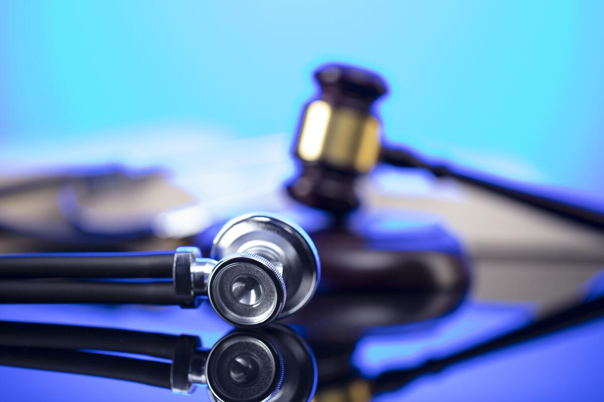 A close-up of a doctor's stethoscope. in the foreground with a judge's gavel in the background
