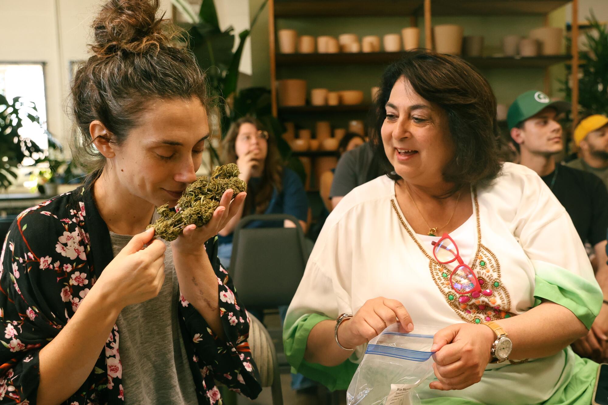 One woman sniffs a large bud of cannabis while another looks on.