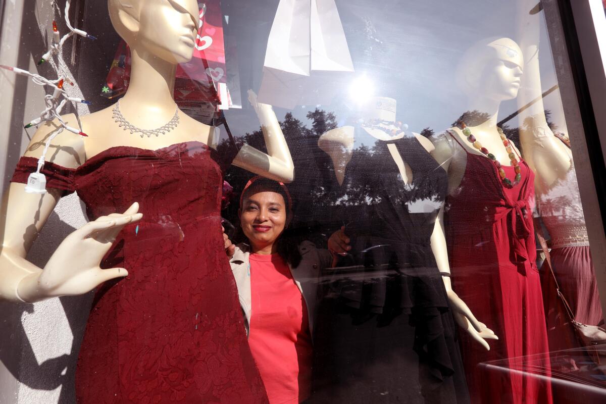 A woman stands between mannequins in a store display window.