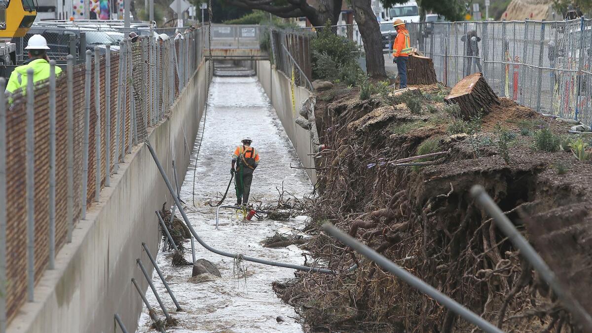 A cleanup worker walks in a storm channel along Laguna Canyon Road in Laguna Beach on Friday after part of a flood wall collapsed during Thursday’s rainstorm.