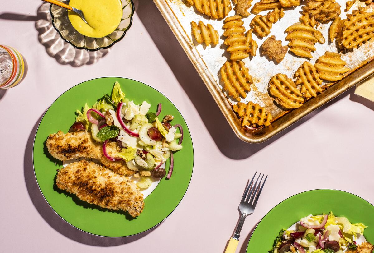 An overhead view of plates with pieces of baked chicken and salad with sliced red onion and halved grapes.