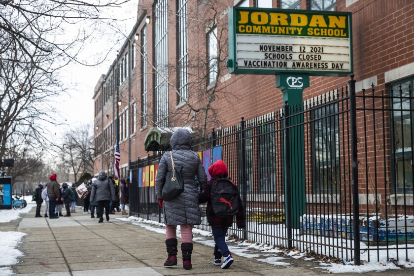 A woman and a child walk past a fence near a brick building with a sign that reads Jordan Community School