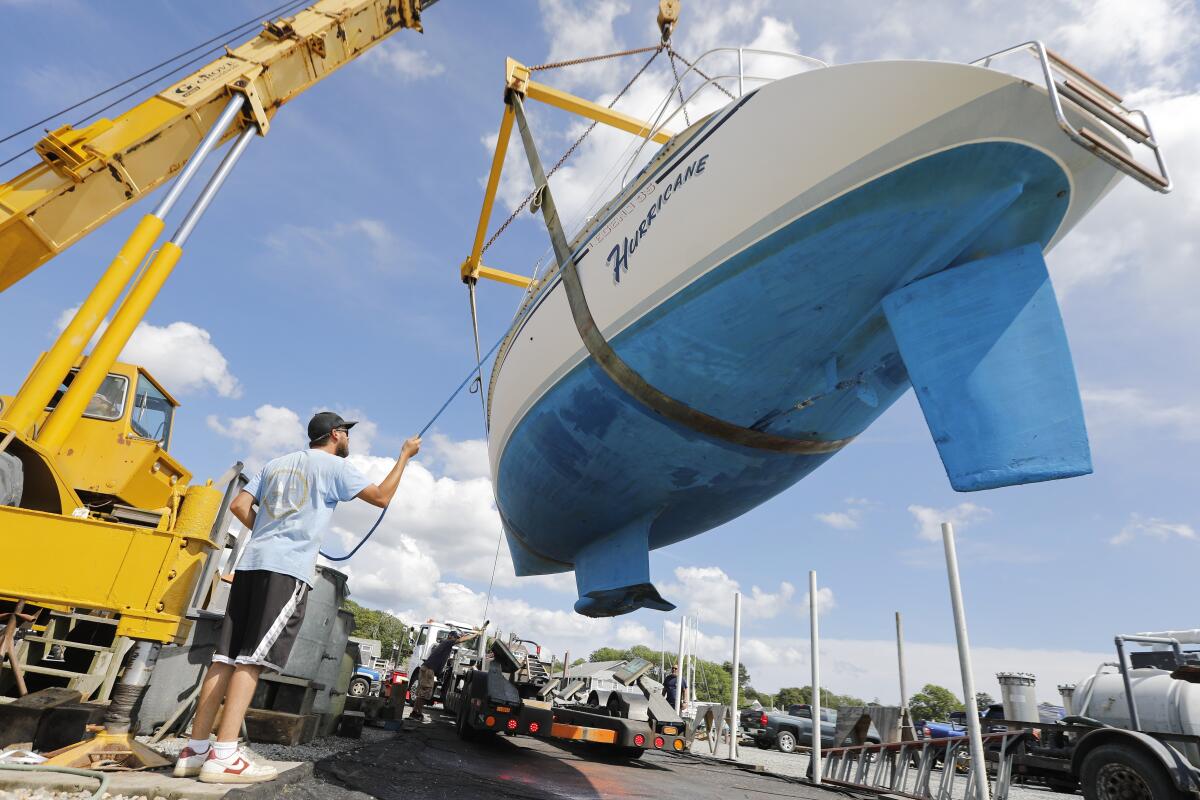 A man stands next to a crane pulling a sailboat named Hurricane from the waters of Padanaram Harbor.