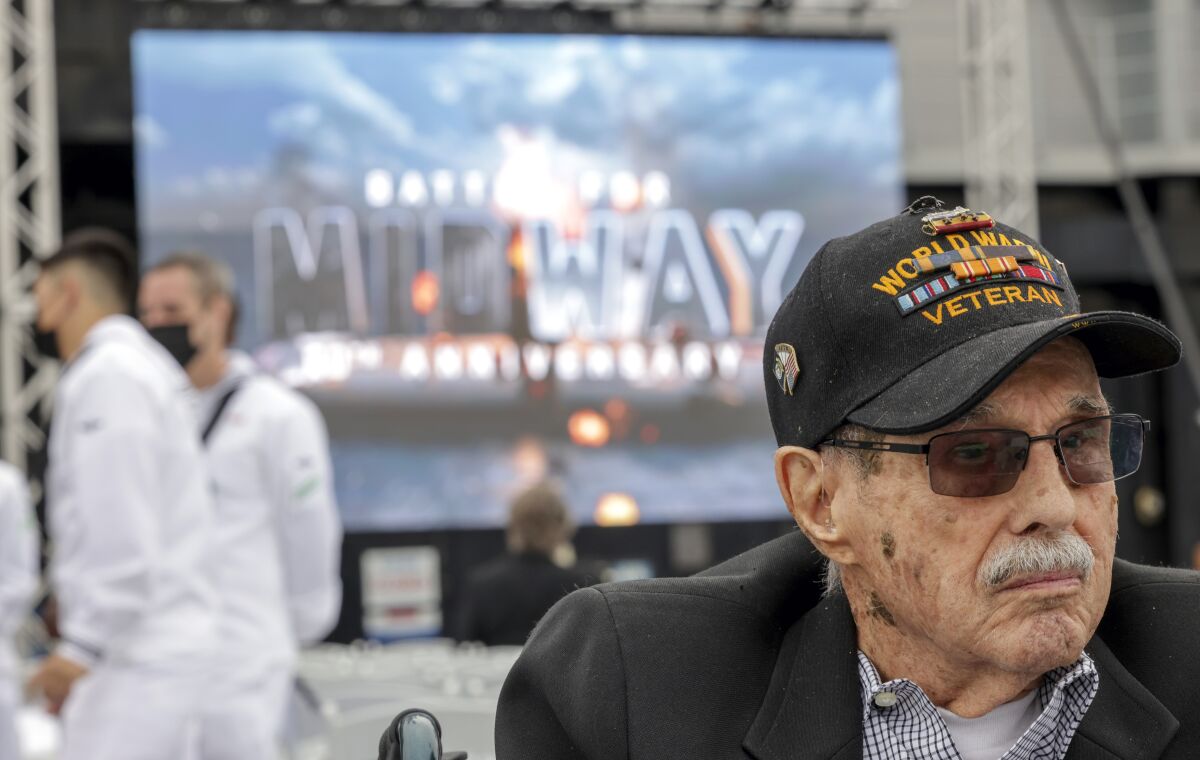 Battle of Midway veteran Charles Monroe sits as a video shows images behind him