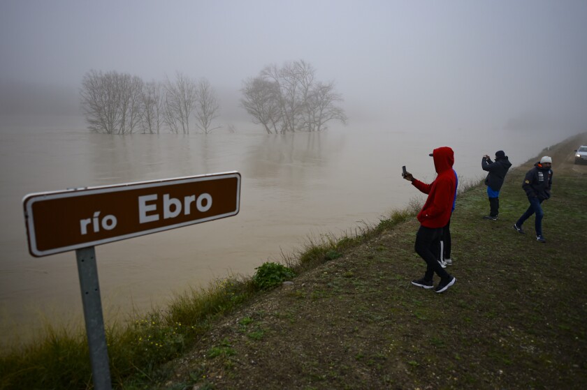 People stand beside the border of flooded area near the Ebro River in the small village of Pradilla de Ebro, Aragon province, northern Spain, Monday, Dec.13, 2021. Heavy rain has led to flooding in northern Spain. (AP Photo/Alvaro Barrientos)