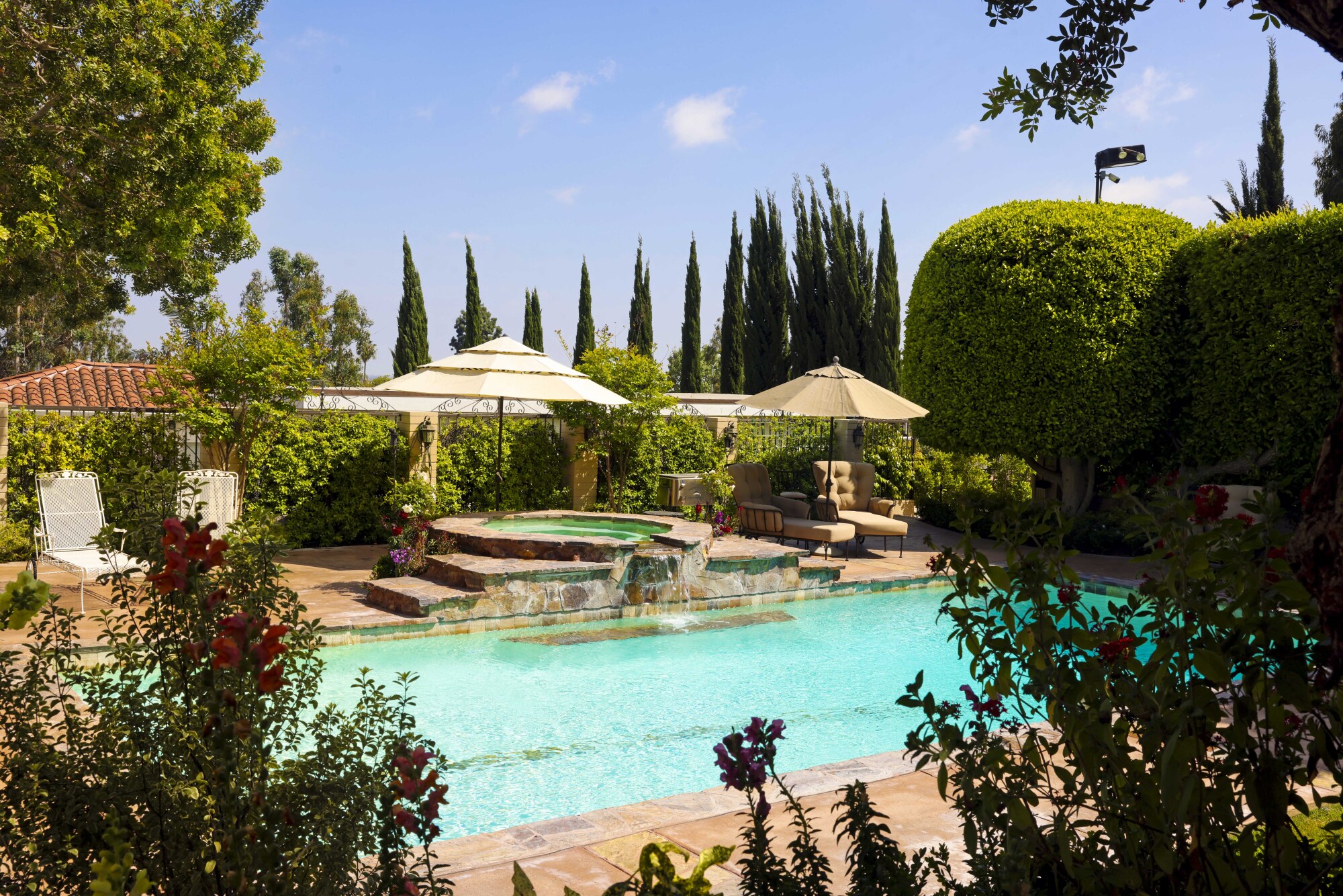 A pool with a fountain surrounded by bushes and trees 