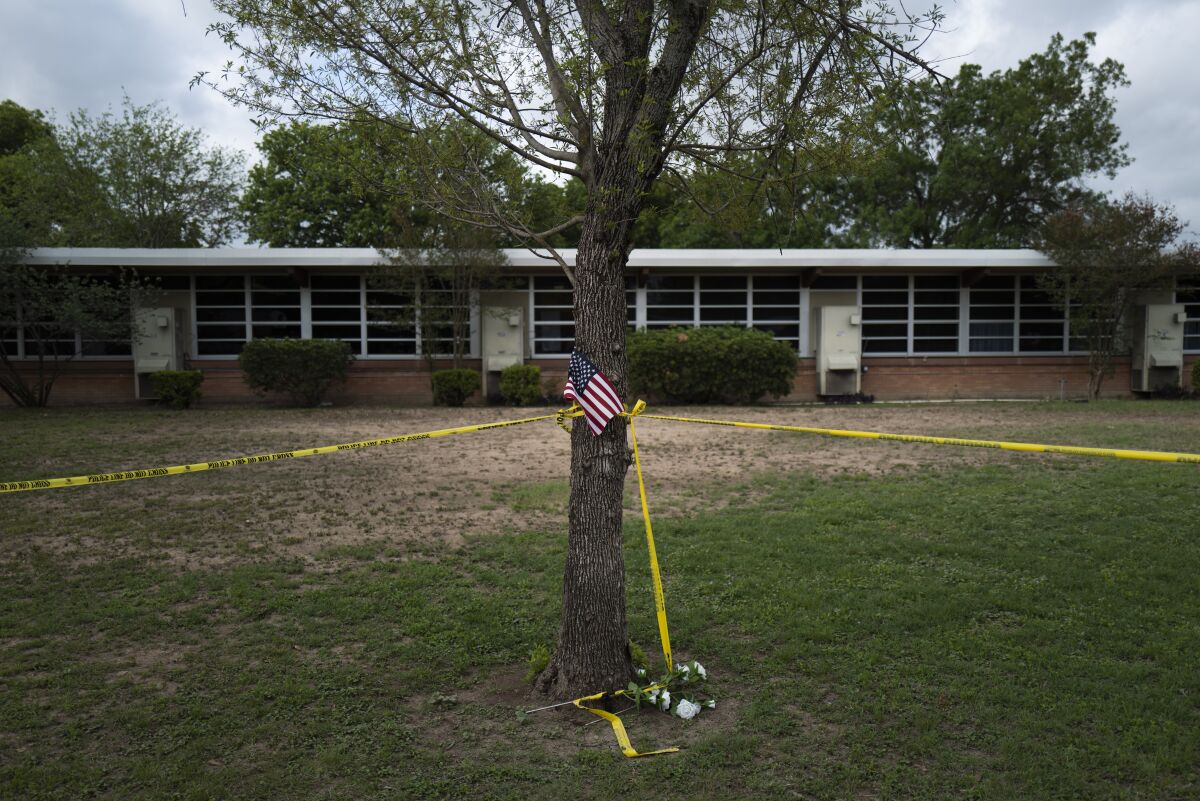A school building stands behind a tree with an American flag and crime scene tape at Robb Elementary School in Uvalde