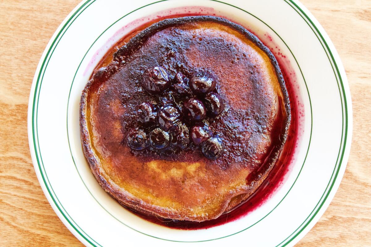 An overhead photo of brown-butter pancakes with blueberry compote on a wooden table