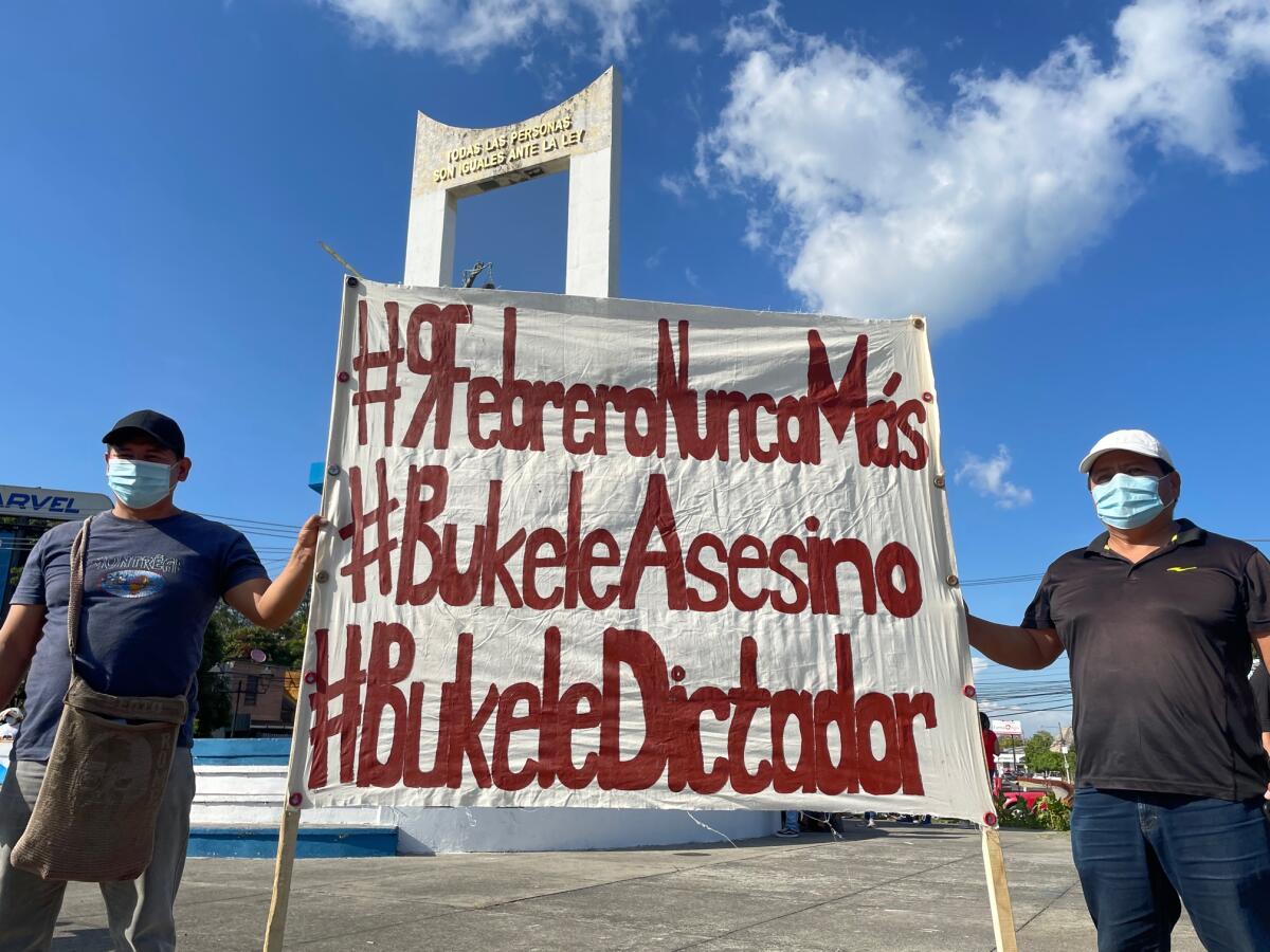 Two people hold a sign denouncing El Salvador's president