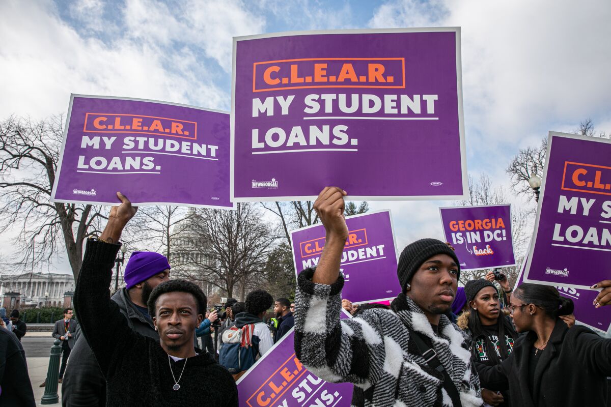 Demonstrators hold signs reading "Clear my student loans."