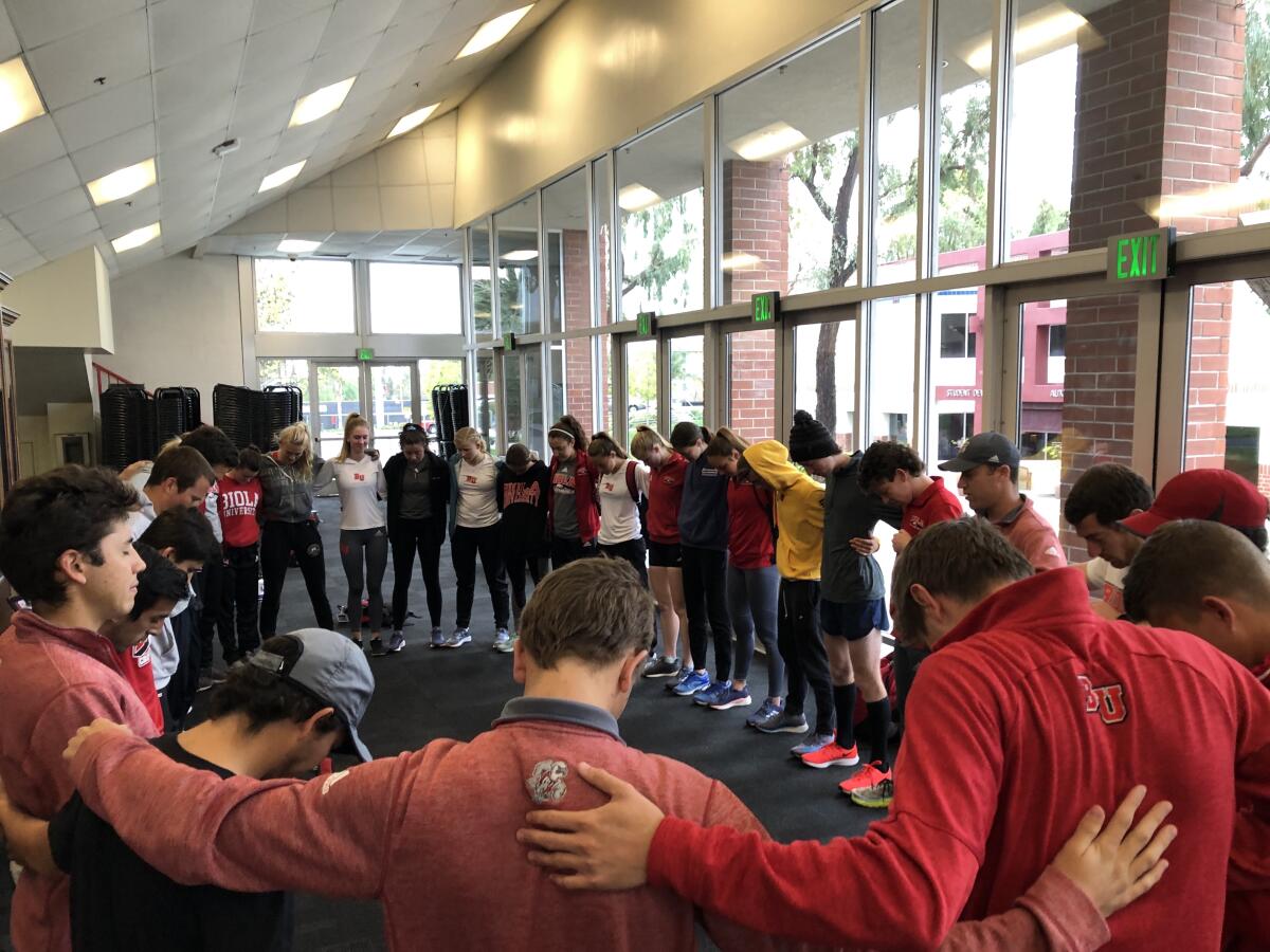 Biola University distance runners listen to coach Sean Henning, at right in a gray hat, before a workout March 14, 2020, in La Mirada. 