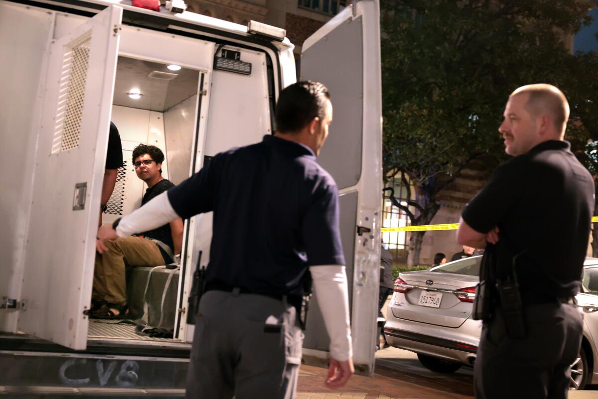 An arrested person is seen in the open back of a van. 