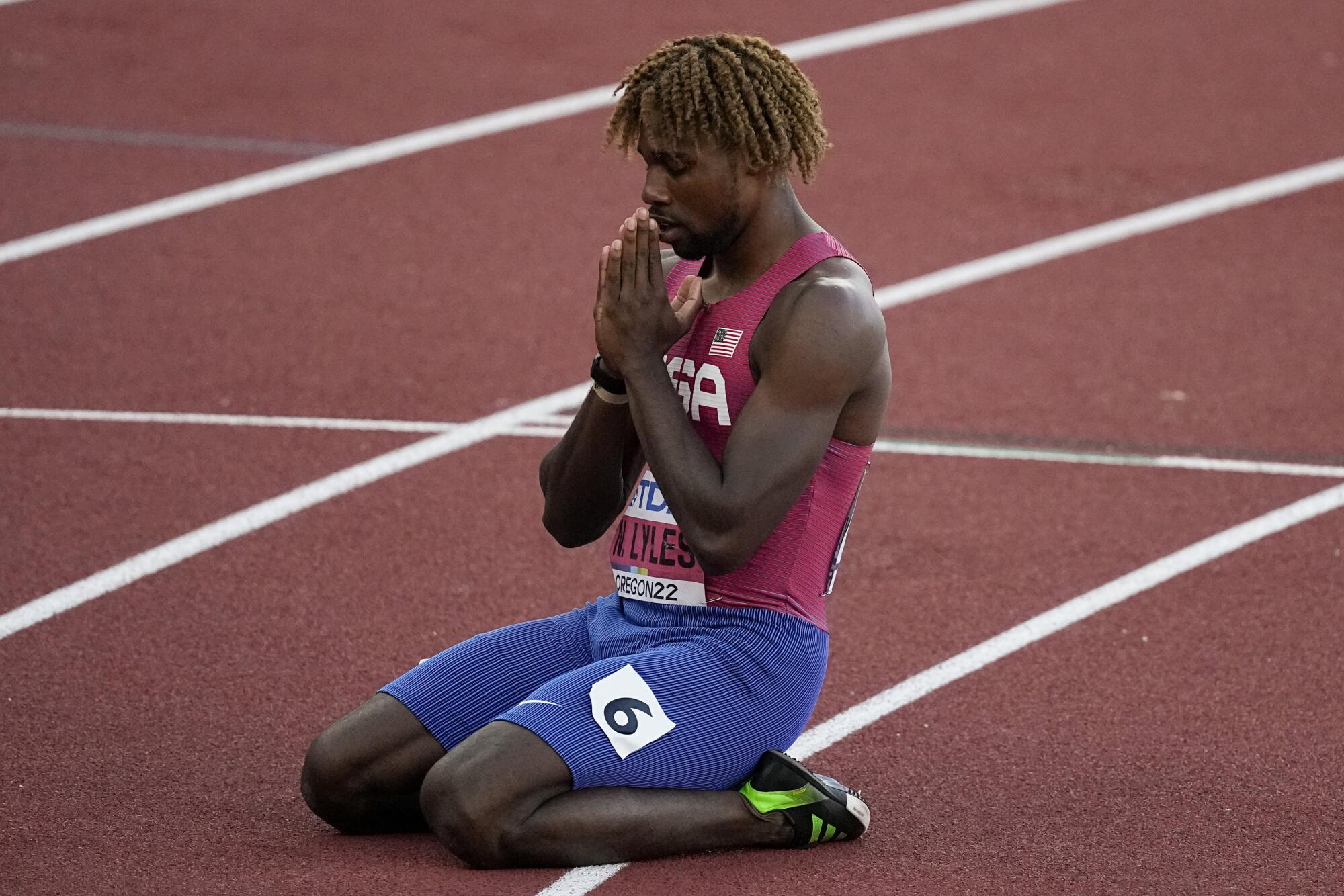Noah Lyles kneels on the track with his hands clasped in prayer after winning the 200-meter dash at the world championships.