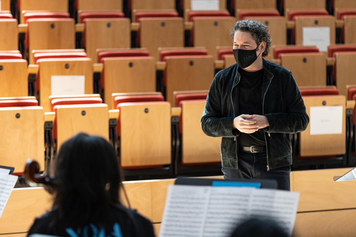 Gustavo Dudamel wears casual clothes as he stands in front of musicians in an empty concert hall