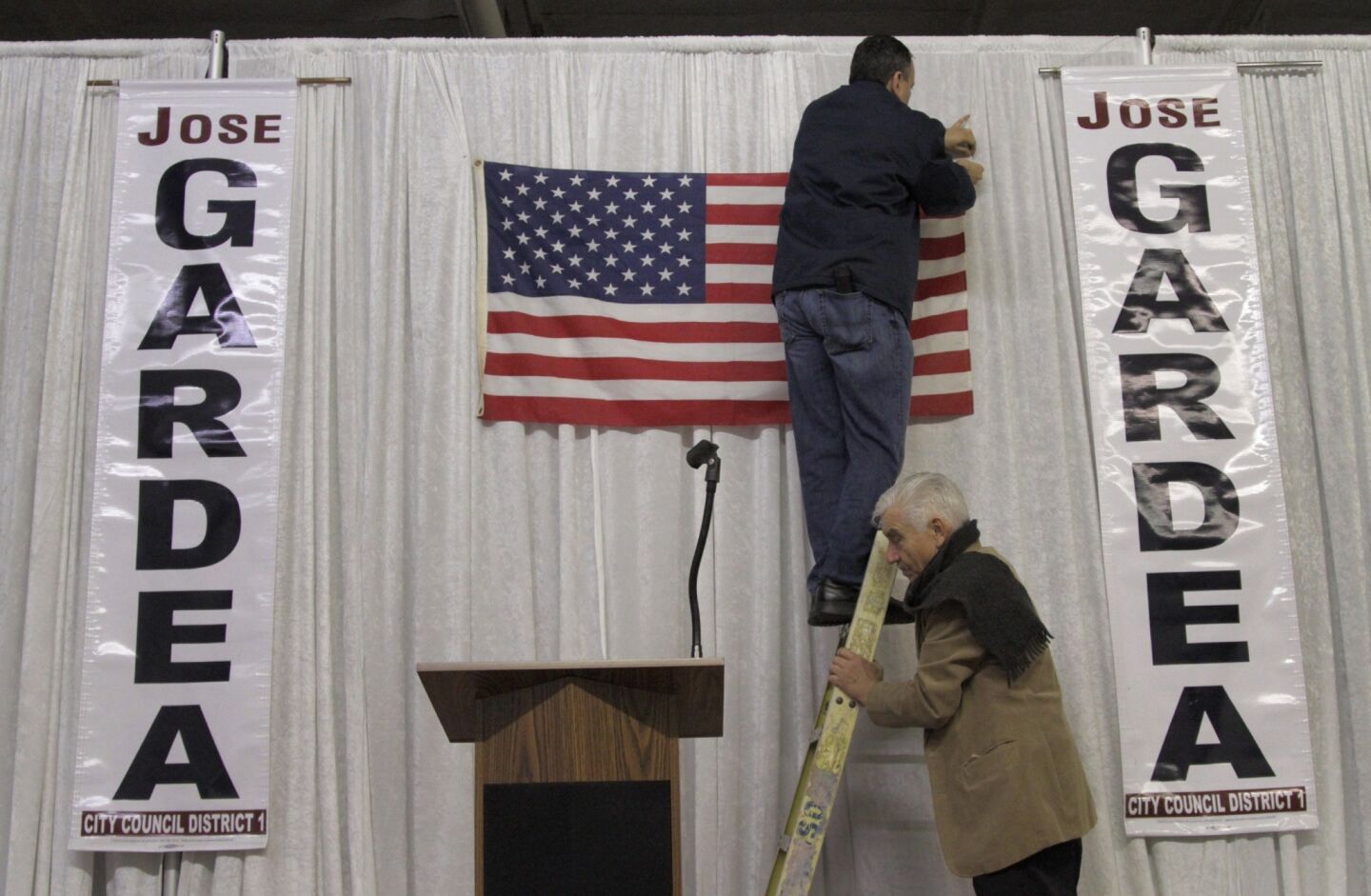 Campaign supporter Eric Ortiz hangs a flag as Guadalupe Davalos steadies the ladder at Jose Gardea's campaign party space in Los Angeles.