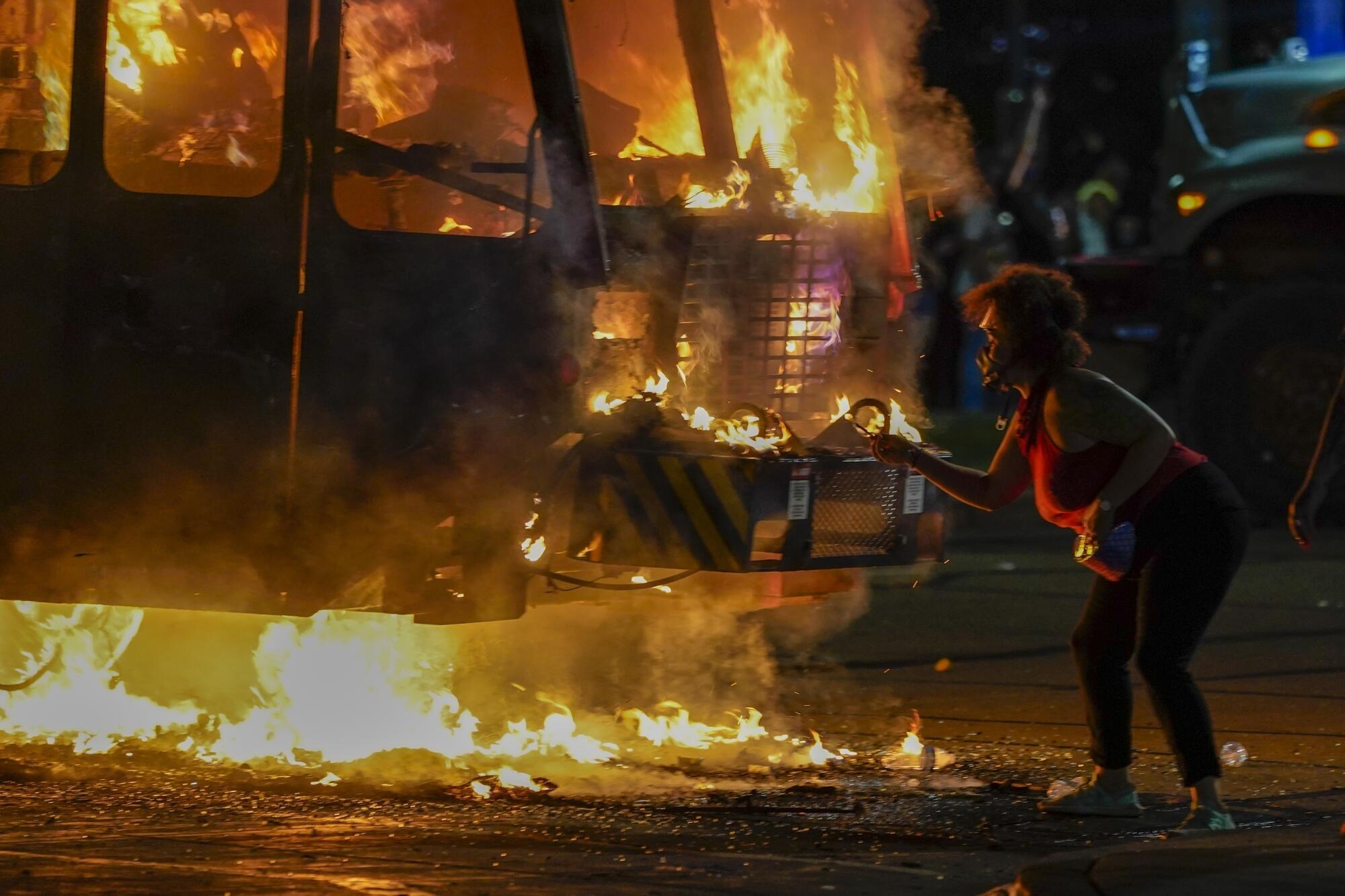 A protester lights a cigarette on a garbage truck that was set on fire.