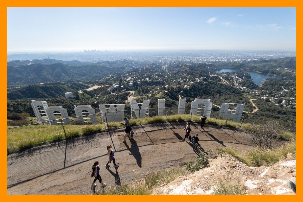 Pedestrians walk behind the Hollywood sign on Mt. Lee Drive.