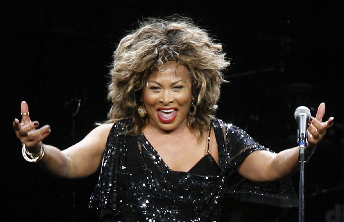 Tina Turner in a black sparking dress holding her hands out in front of her