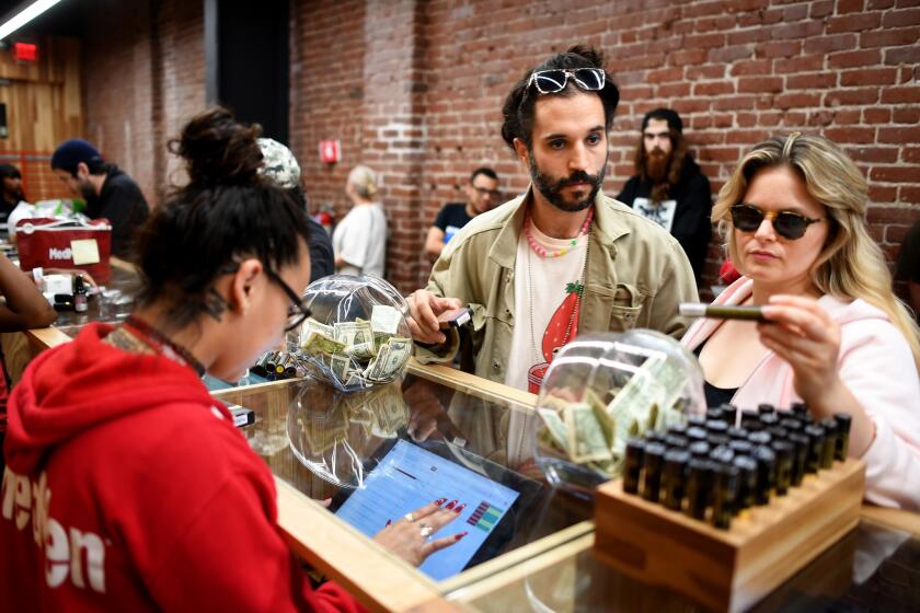 LOS ANGELES, CALIF. -- TUESDAY, MAY 22, 2018: Greg Anastasio, right, sales assistant, shows customer Vikas Desai, of New York, flower strains of marijuana at MedMen, marijuana and marijuana products retail store, in Los Angeles, Calif., on May 22, 2018. MedMen, a Culver City cannabis company that has about a dozen pot shops and a handful of grow operations, is going public. (Gary Coronado / Los Angeles Times)