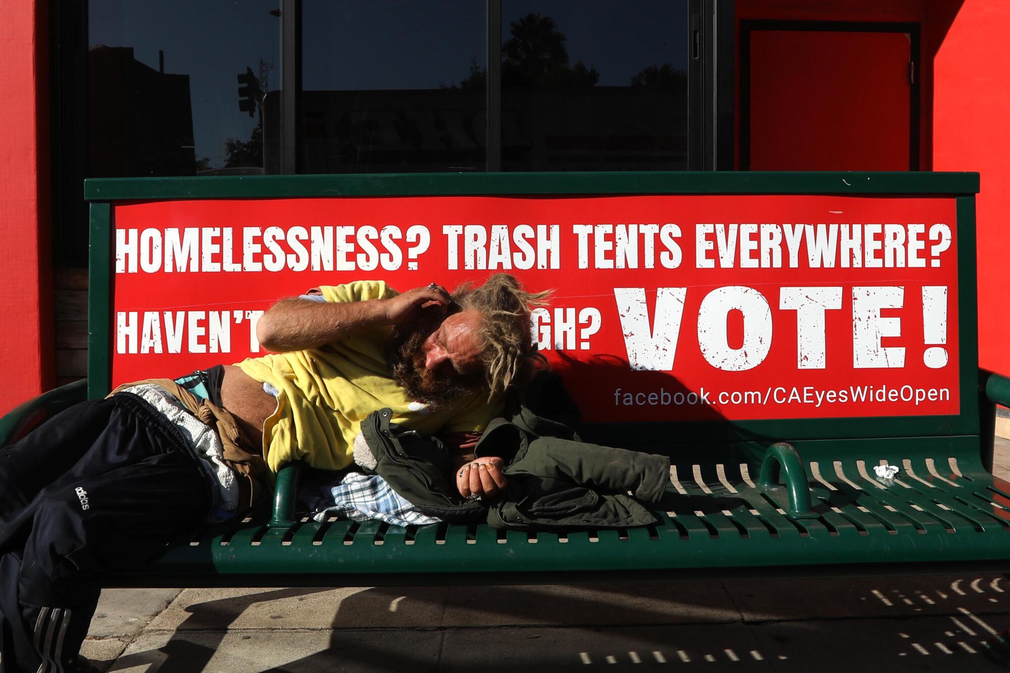 A homeless man in Santa Monica rests on a bench featuring a voting advertisement Monday.