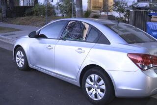 A silver Chevy sedan had its rear driver side window completely smashed in; the vehicle owner had since covered the damage with what appeared to be a piece of cardboard, part of a garbage bag and tape. (KTLA)