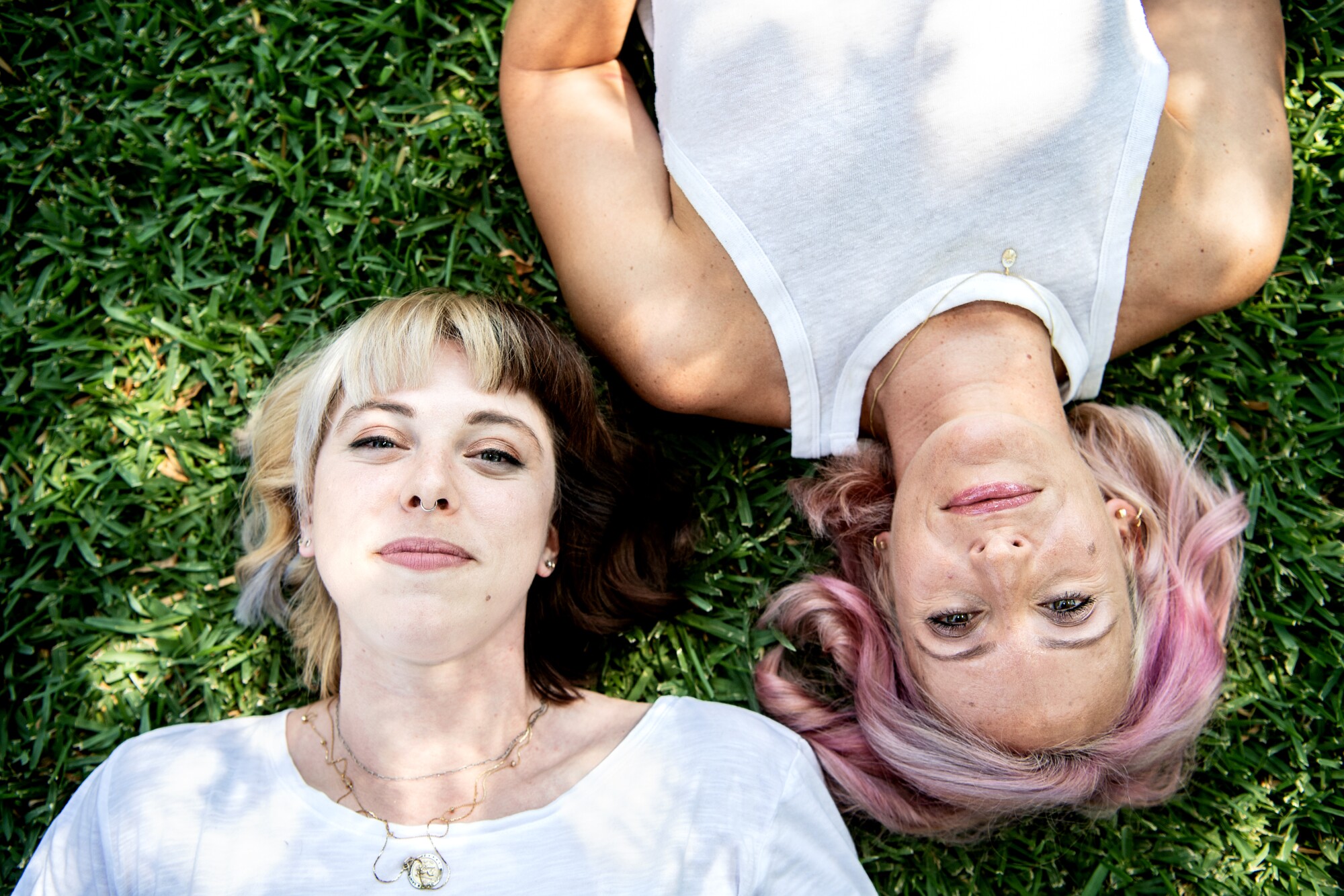 Two women lie on grass in the shade.