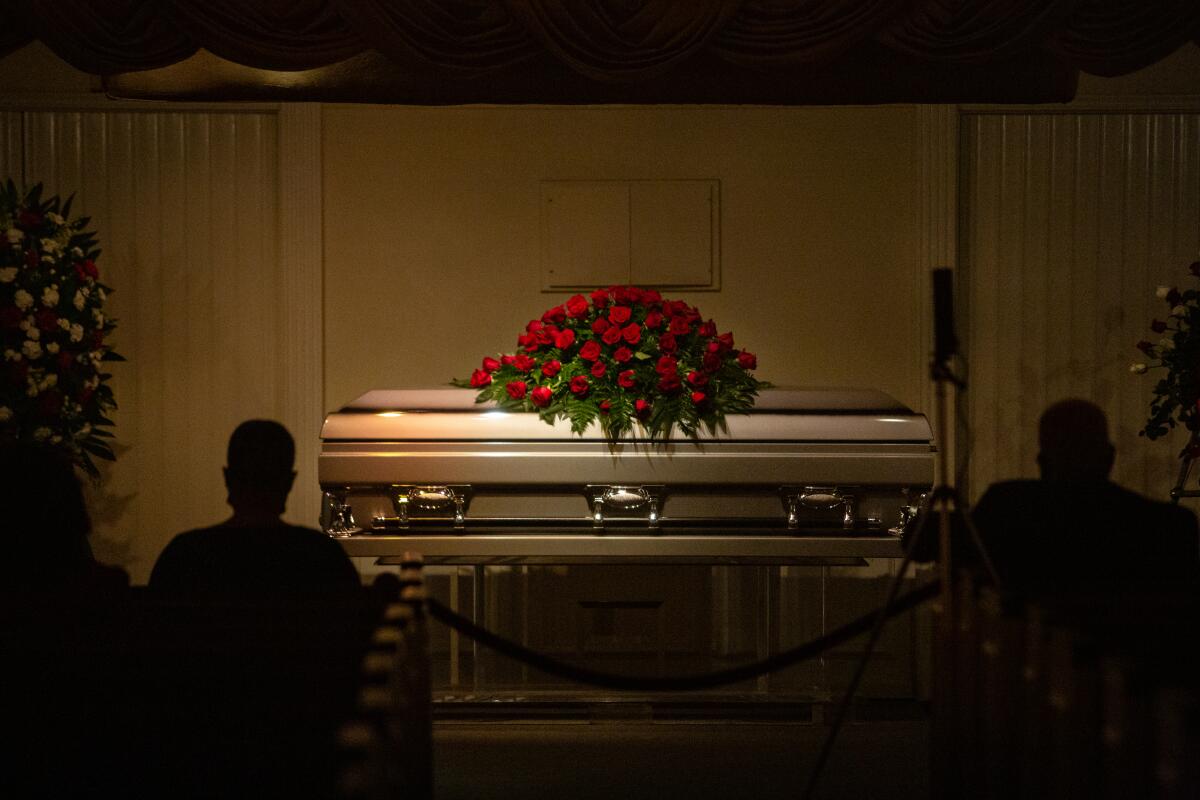 A coffin is shown with two people seated on each side of it.