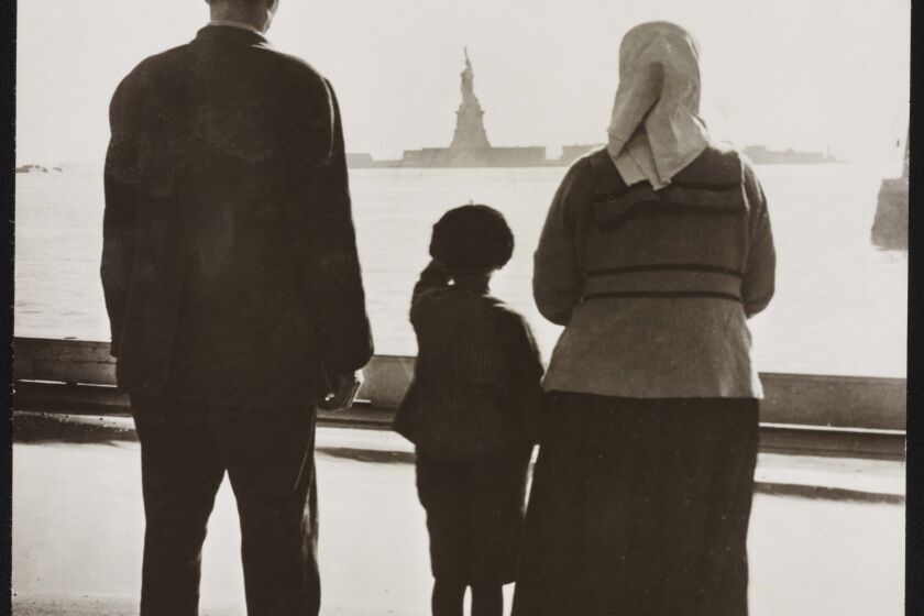 Photo shows immigrant family looking at Statue of Liberty from Ellis Island. c1930