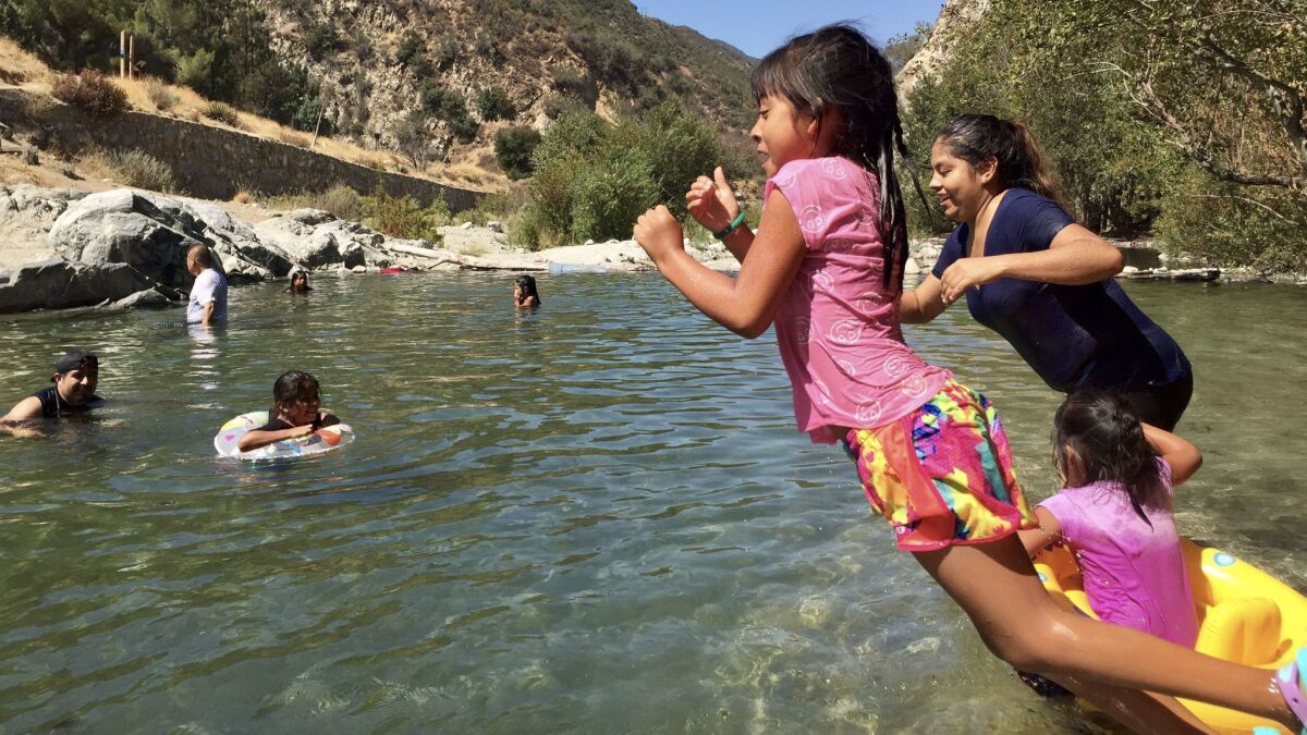 After traveling from Orange County for the day, Dioselin Romero, center and Isabel Flores leap from banks of East Fork of San Gabriel River.