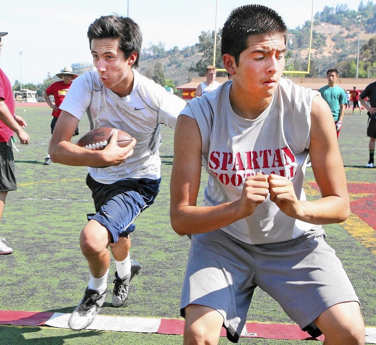Daniel McGowin carries the ball past Bryan Soto's block during a La Cañada High School football team spring practice on Tuesday, May 27, 2014. This is head coach Ramsey Lambert's first season.