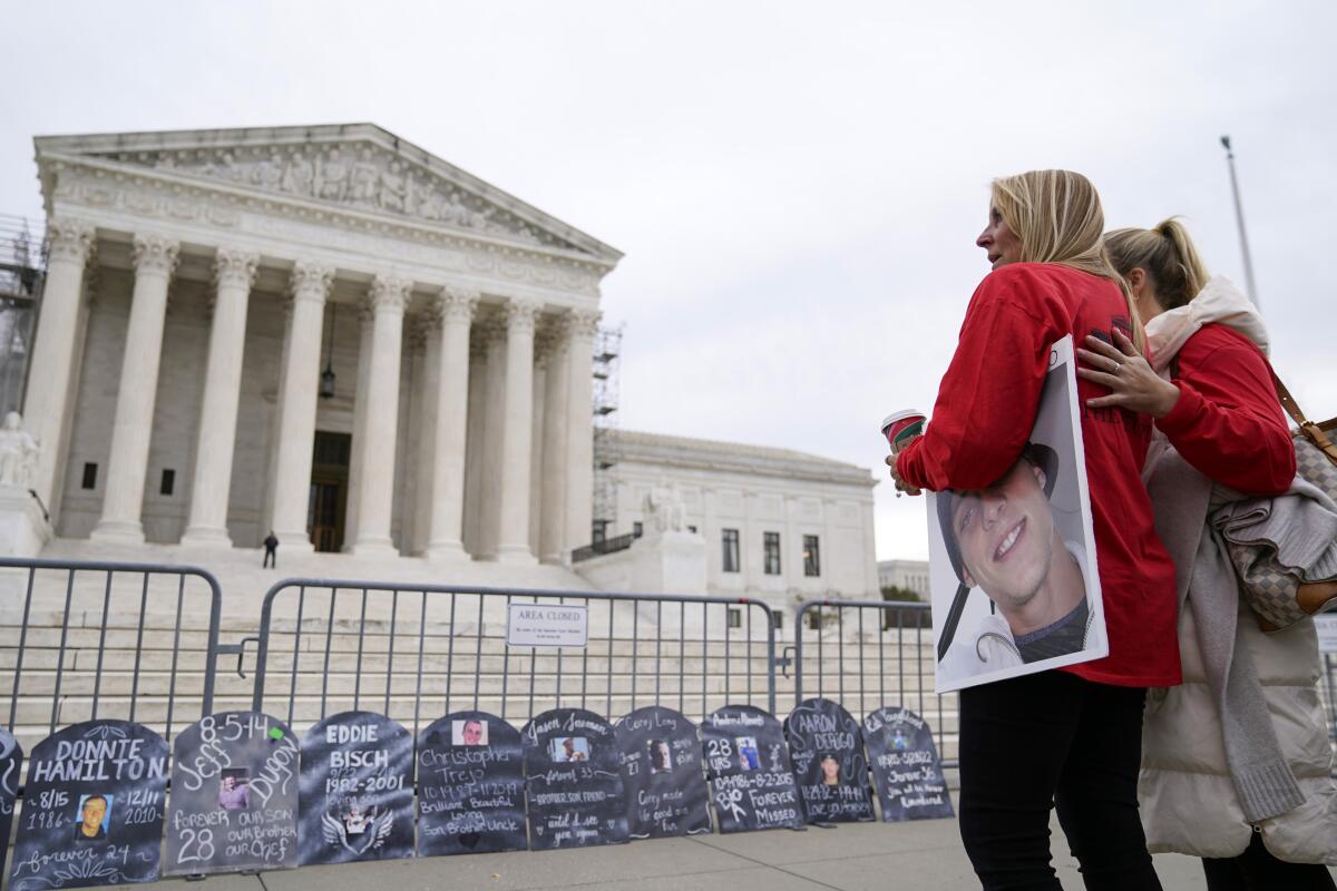 Two women, one holding a picture, outside the Supreme Court. "Gravestone" markers lean against a barricade.