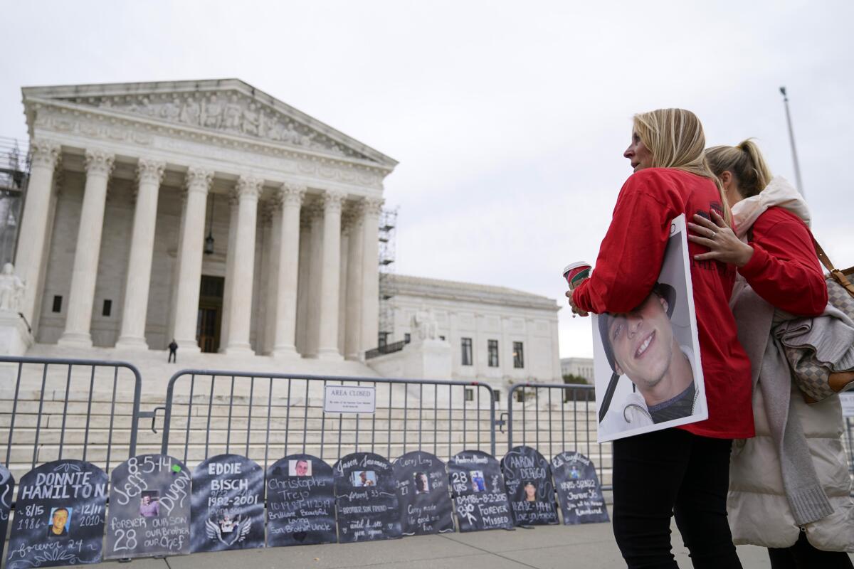 Two women, one holding a picture, outside the Supreme Court. "Gravestone" markers lean against a barricade. 