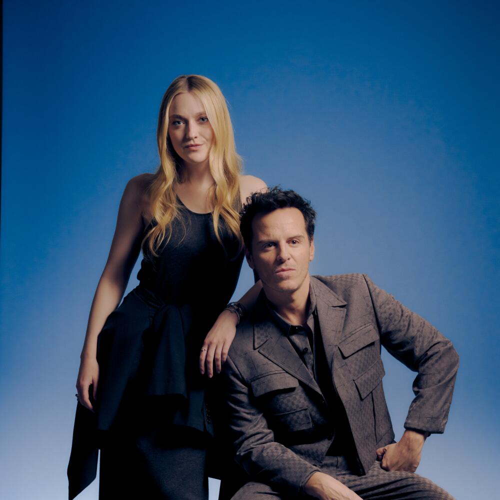 A woman in a long, dark dress leans against the shoulder of a man who is sitting on a stool.