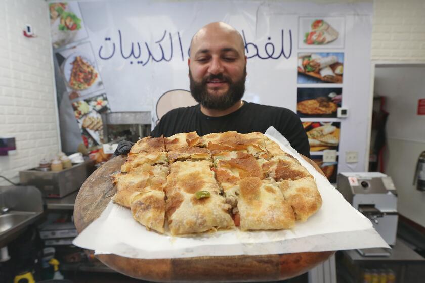 Owner and chef Sam Zarzour stands in the dining room holding a popular beef shawerma pie at his Feteer Guy, a new restaurant serving up savory Egyptian pizza pies and desserts in Huntington Beach.