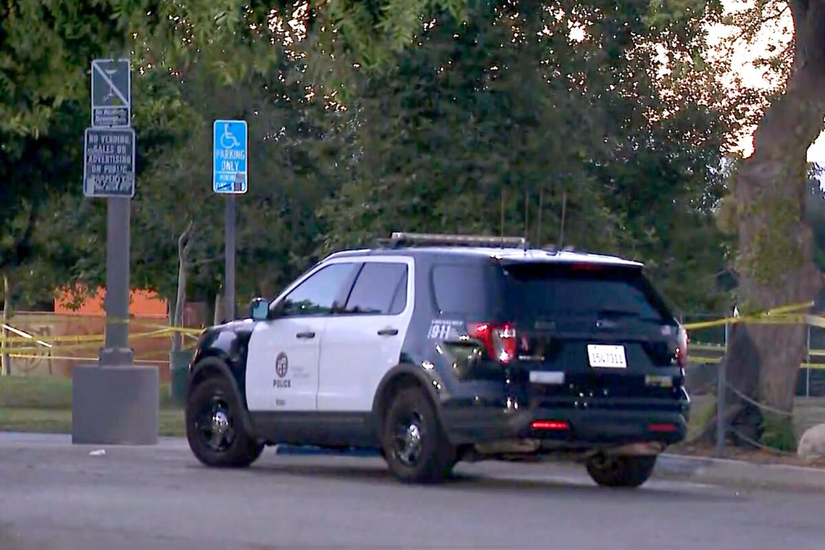 A police SUV stands next to a park with an area blocked off by police tape. 