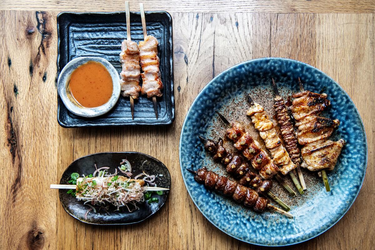 Various kushiyaki skewers from Tsubaki in Echo Park: pork jowl, yakitori and tofu on plates atop a wood table