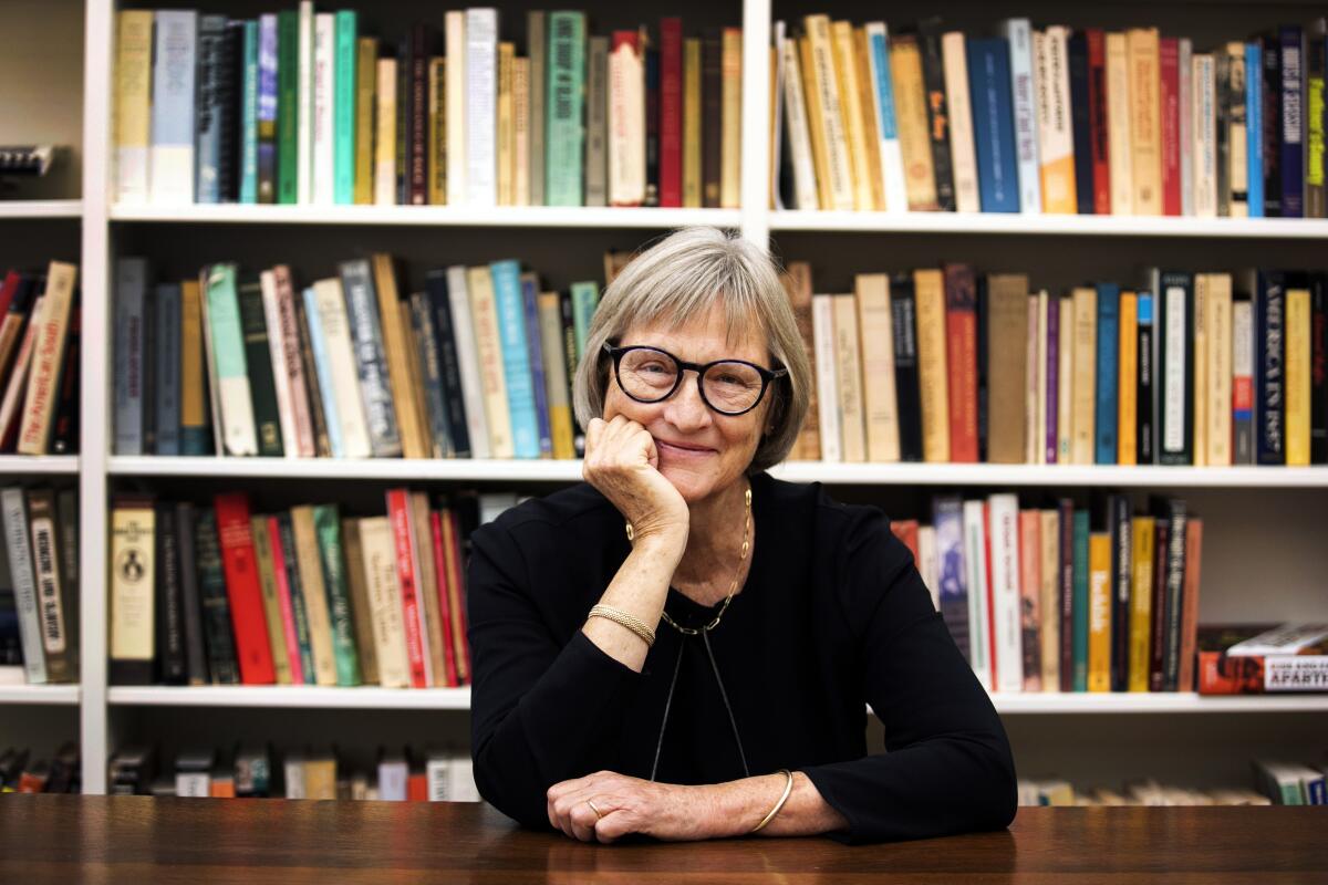 Drew Gilpin Faust wears a black long sleeve and smiles in front of bookshelves.