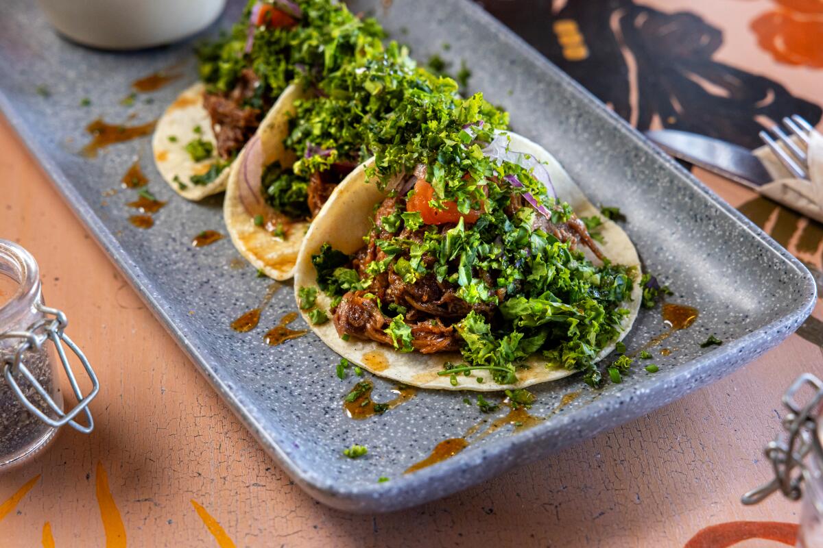Oxtail tacos with roasted tomato, shredded kale and whiskey reduction on a rectangular dish