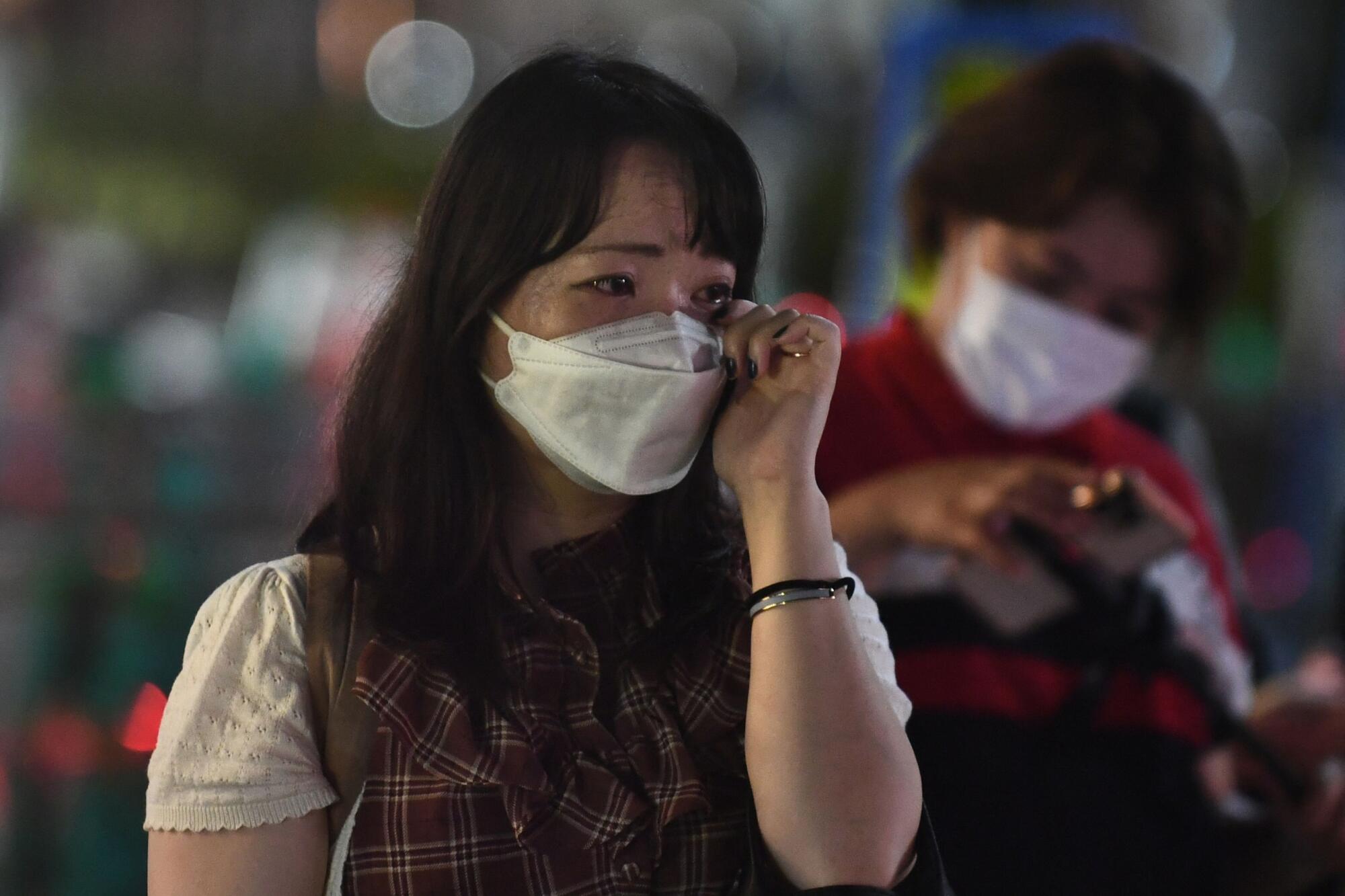 A woman wipes away tears in front of a makeshift memorial for Abe