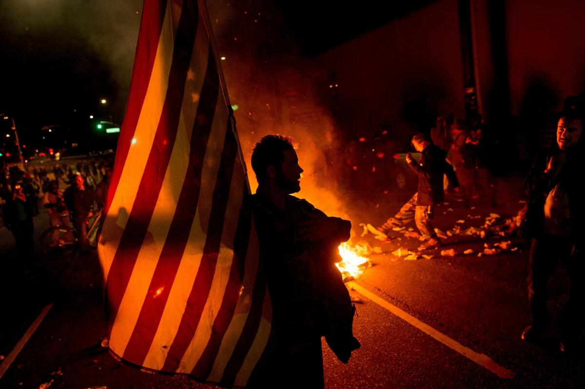 James Cartmill holds an American flag while protesting in Oakland, Calif., on Monday, Nov. 24, 2014, after the announcement that a grand jury decided not to indict Ferguson police officer Darren Wilson in the fatal shooting of Michael Brown, an unarmed 18-year-old. Several thousand protesters marched through Oakland with some shutting down freeways, looting, burning garbage and smashing windows. (AP Photo/Noah Berger) The Associated Press